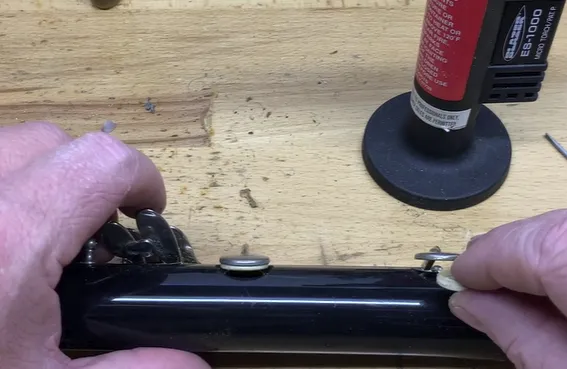 Screenshot 2024-09-03 134240 A close-up photo of a clarinet with a missing pad, with the fallen pad and the required tools - a micro torch and small screwdriver - laid out next to the clarinet, clarinet pad replacement