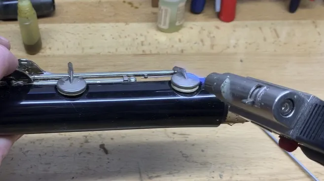 Screenshot 2024-09-03 134334 A close-up shot of a person's hand holding a micro torch, applying heat to the side of a clarinet's pad cup. clarinet pad replacement
